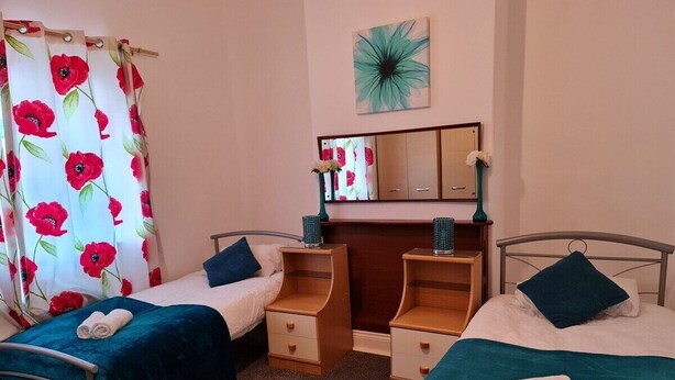 Una camera da letto con due letti singoli, un comodino in legno, una cassettiera e uno specchio sopra la cassettiera.