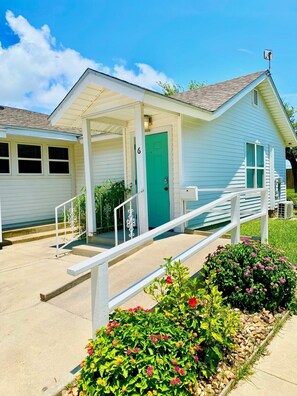 A single-story building with a green door, a covered porch, and a white railing. - Coast Oaks Cottage 6 1 Bedroom Cottage by RedAwning (Rockport)
