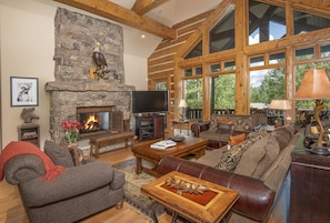 A spacious living room with a stone fireplace, wooden beams, large windows, and a cozy seating area. - 40 Goshawk 5 Bedroom Home by RedAwning (Avon)