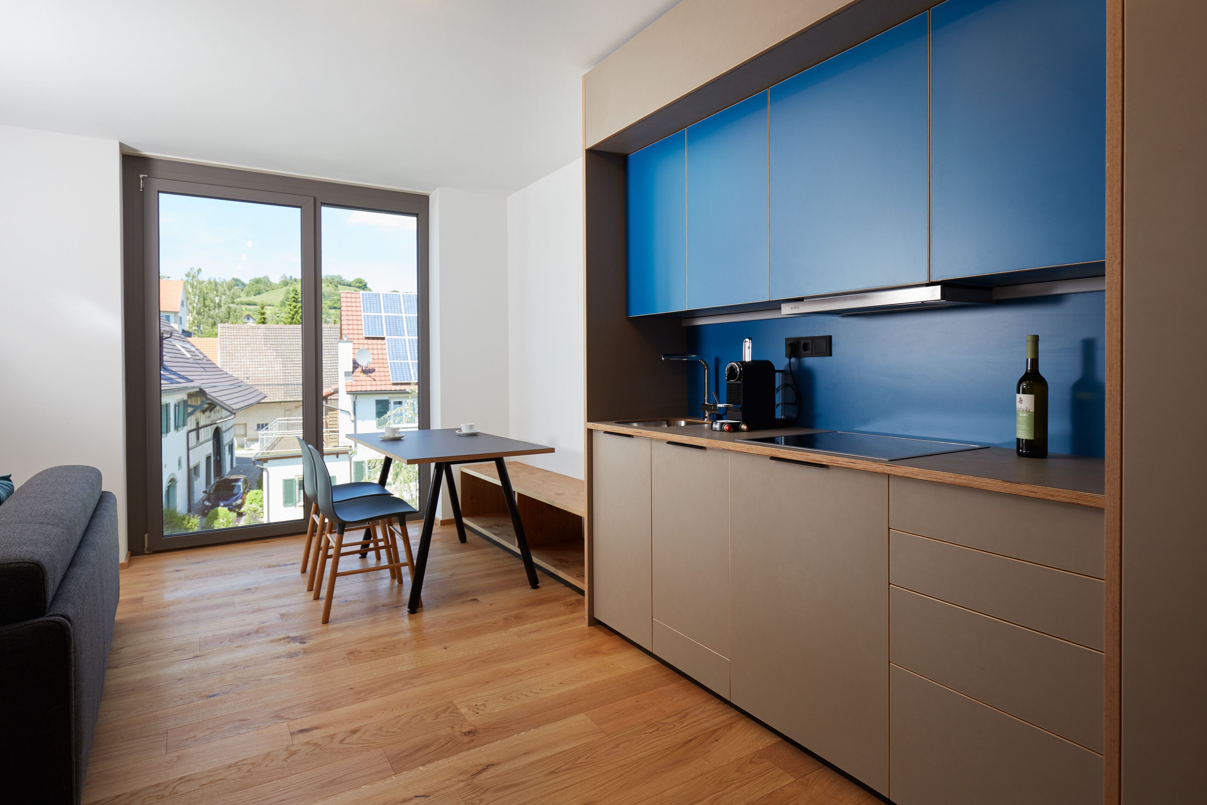 A modern kitchen with blue cabinets, a dining area with a table and chairs, and a view through a glass door.