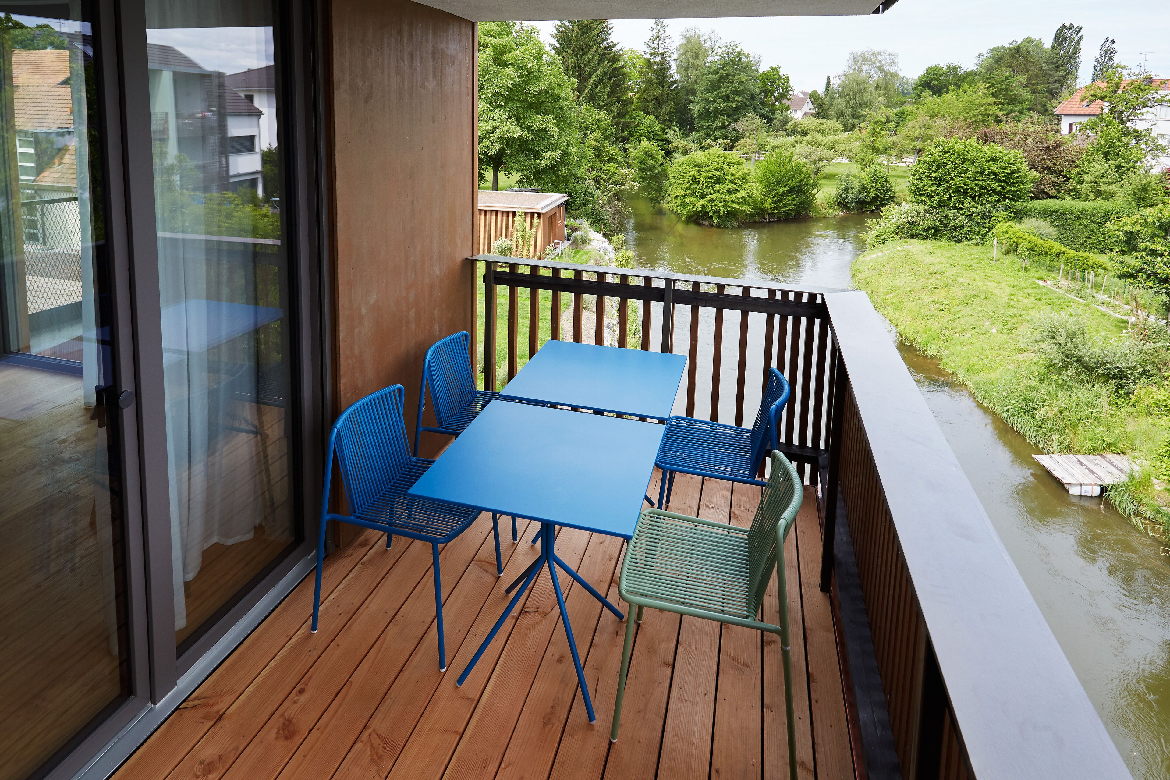 A balcony with a wooden floor, a blue table, and green chairs.