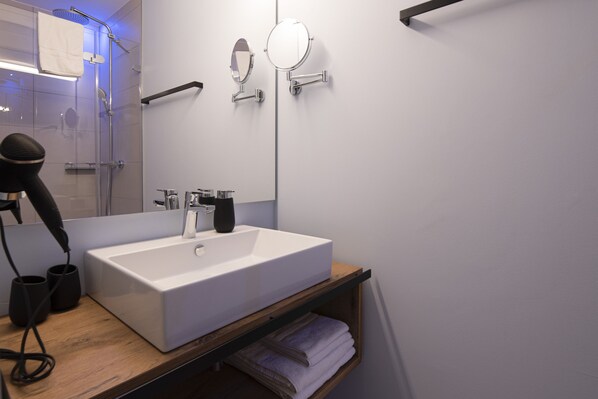 Ein modernes Badezimmer mit einem großen, weißen Waschbecken, einem Handhaartrockner und zwei Spiegeln an der Wand.