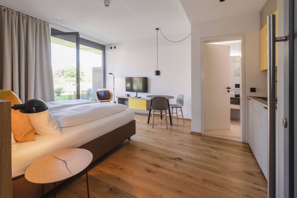Ett modernt hotellrum med en stor säng, ett skrivbord, en TV och utsikt över omgivningarna.