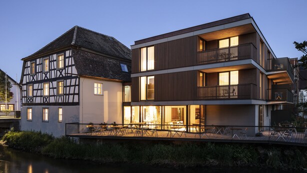 Un edificio moderno con un balcón y una estructura tradicional de entramado de madera a su lado.