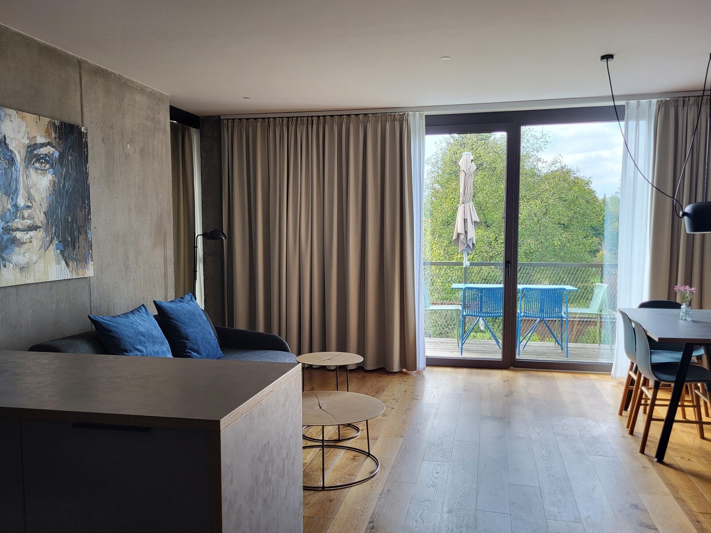 Una sala de estar moderna con un sofá, una mesita redonda y un balcón con mobiliario exterior.