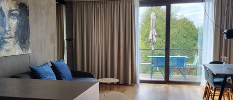 Una sala de estar moderna con un sofá, una mesita redonda y un balcón con mobiliario exterior.