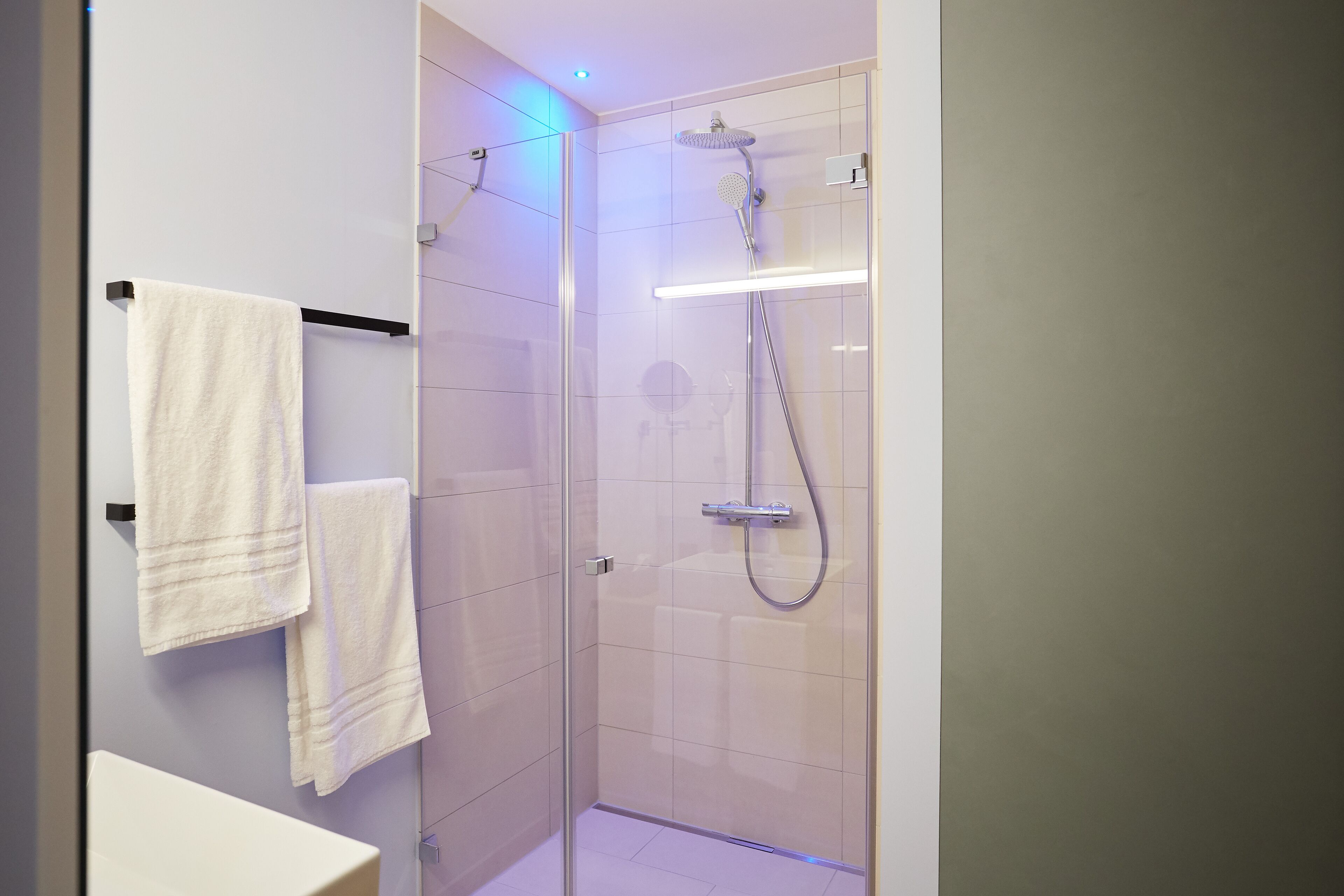Uma casa de banho moderna com chuveiro em cabine de vidro, lavatório branco e duas toalhas penduradas num suporte.