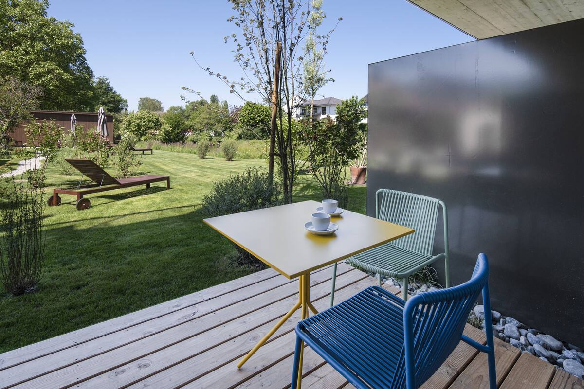 En terrass med ett bord och stolar, med utsikt över en välskött gräsmatta och ett hus i bakgrunden.