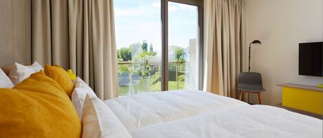 A hotel room with a large bed, a desk, a chair, a TV, and a balcony with curtains.