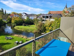 A balcony with a view of a river, houses, and a church steeple. - Sternen Bohlingen Aparthotel (Singen)