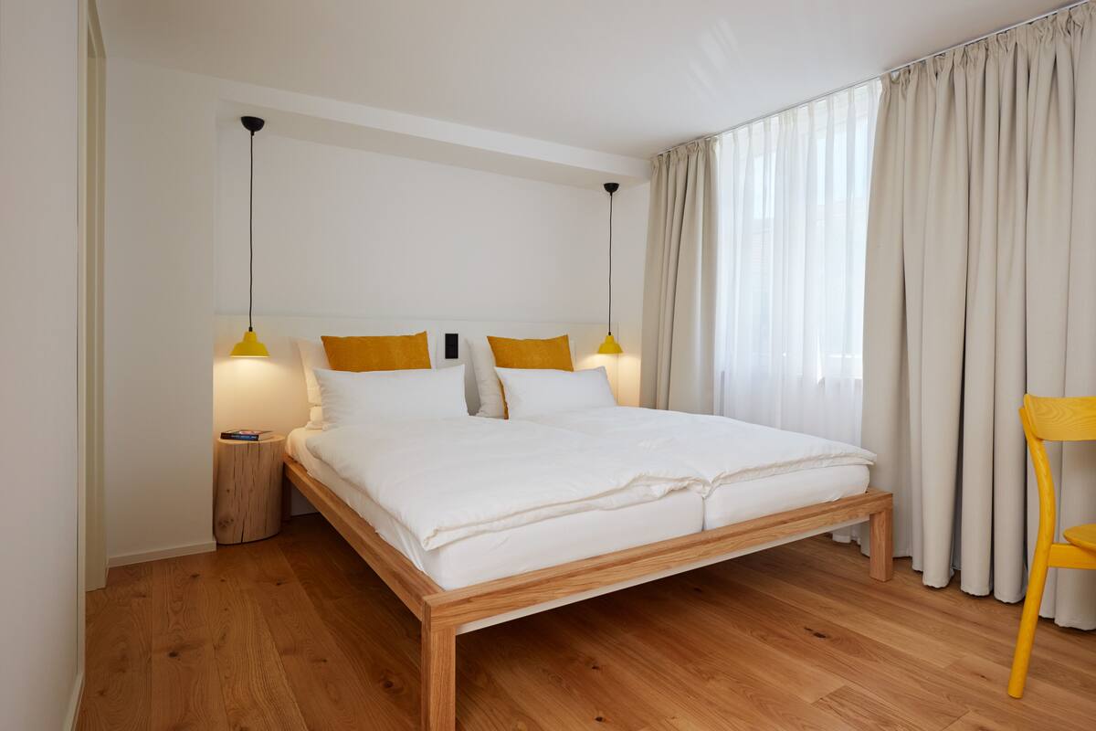 Ett modernt sovrum med en säng i trä, två sänglampor och en stol.