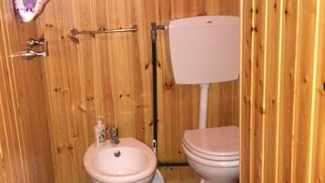 Un baño pequeño con paredes de madera, un inodoro blanco, un lavamanos blanco y un tapete a rayas en el suelo.