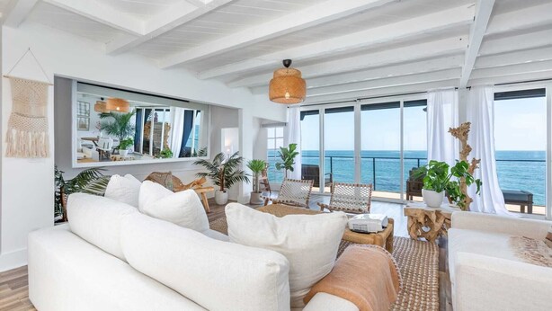 Un vaste espace de vie comprenant un grand canapé, une table à manger et des chaises. Une grande fenêtre offre une vue sur la mer.