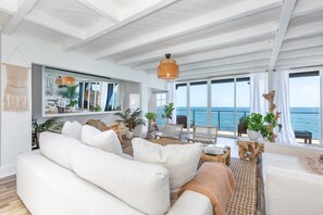 A spacious living area with a large sofa, a dining table, and chairs. There is a large window offering a view of the sea. - Casa del Mar by Oraklus (Malibu)