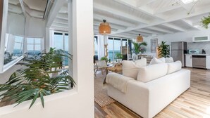 Un vaste espace de vie agrémenté d’un canapé blanc, de parquet et de grandes fenêtres offrant une vue sur l’océan.