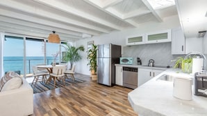 Une cuisine moderne dotée d’un grand îlot central, d’appareils électroménagers en acier inoxydable et offrant une vue sur l’océan.