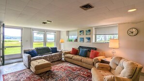 A spacious living room with a large window, a sofa set, a patterned rug, and a clock on the wall.