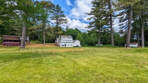 A two-story house surrounded by a grassy field and tall trees.