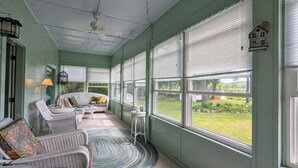 A sunroom with wicker furniture, a ceiling fan, and a view of a green landscape.