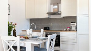 A modern kitchen with white cabinetry, a stainless steel range hood, and a dining area with white chairs and a table set for two. - House Manda Adriatic (Piramatovci)