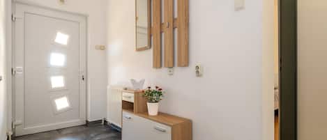 A hallway with a white door, a wooden console table with a potted plant, and a mirror on the wall.
