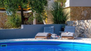 A poolside area with two lounge chairs, a small table with towels, and a stone wall. - House Manda Adriatic (Piramatovci)