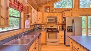 Cocina de cabaña de madera con fregadero, estufa, microondas, refrigerador y ventanas amplias.