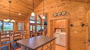 Interior de una cabaña de madera con cocina, comedor y chimenea de piedra.