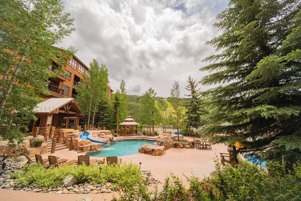 Surrounded by evergreen trees and mountains, this resort features a central pool area with rock formations and seating.