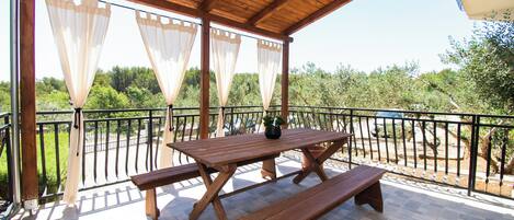 Une terrasse extérieure en bois, dotée d’une table de pique-nique et de bancs, entourée d’une rambarde en métal et de rideaux légers.