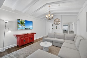 A modern living room with a large flat-screen TV, a red cabinet, a beige sofa, and a white coffee table.