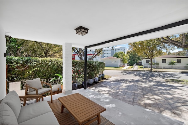 A covered outdoor seating area with a sofa, chairs, and a table.