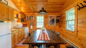 Una cocina estilo cabaña de madera con una mesa de comedor central, armarios de madera y una lámpara colgante.