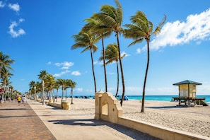 Una playa con palmeras, una torre de salvavidas y un paseo marítimo pavimentado.