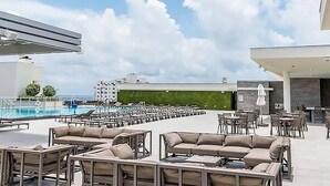 A rooftop pool area with lounge chairs and tables, a swimming pool, and a view of the city skyline.