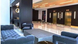 A modern lobby with a seating area, a reception desk, and elevators.