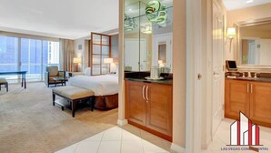 A hotel room with a large bed, a sitting area with a chair and a small table, a kitchenette with a countertop and cabinets, and a large mirror above the sink. - F1 Track + Strip View Studio Suite with Balcony (Las Vegas)