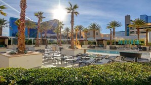 A rooftop pool area with lounge chairs and palm trees, surrounded by modern buildings. - F1 Track + Strip View Studio Suite with Balcony (Las Vegas)