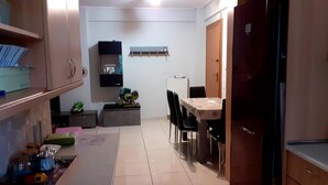 A compact kitchen with a refrigerator, a dining table with chairs, and a small countertop with jars and a toy. - Immaculate 2-bed Apartment (Paiania)