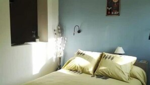 A bedroom with a bed, a wall-mounted clock, and a window with curtains. - CHARMING 2 ROOM APARTMENT WITH ALL COMFORTS + AIR CONDITIONING (Tornac)