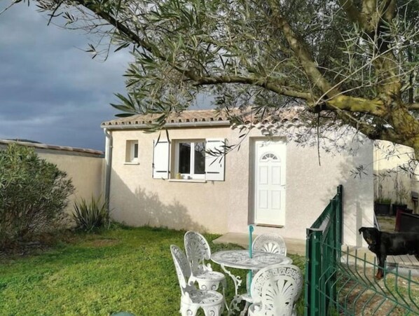A small house with a white exterior, a tiled roof, and a front door. There is a small patio with a table and chairs.
