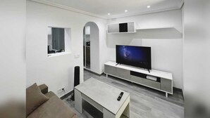 A modern living room with a flat-screen TV, a sofa, a coffee table, and built-in shelving.