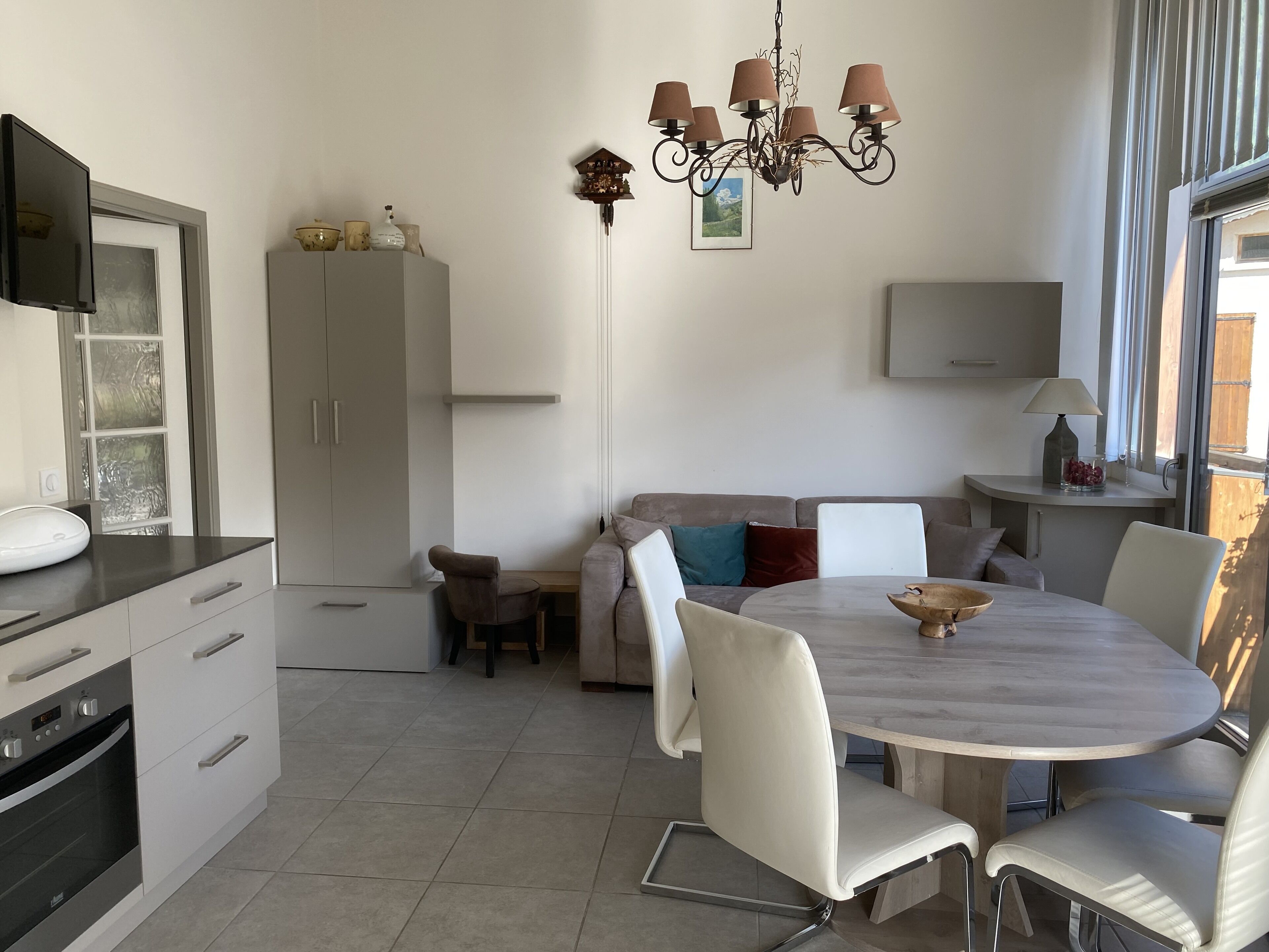 A modern kitchen with a dining area, including a round table and chairs, a built-in oven, and a white cabinet.