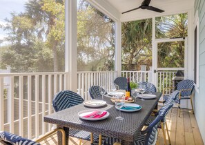 A covered outdoor dining area with a table set for two, surrounded by wicker chairs, and overlooking a lush garden. - Stay @ Mimosa Manor - Private Pool, Steps to Beach (Folly Beach)