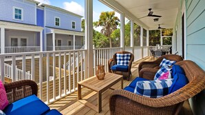 A covered outdoor deck with wicker furniture, a table, and a view of a blue house. - Stay @ Mimosa Manor - Private Pool, Steps to Beach (Folly Beach)