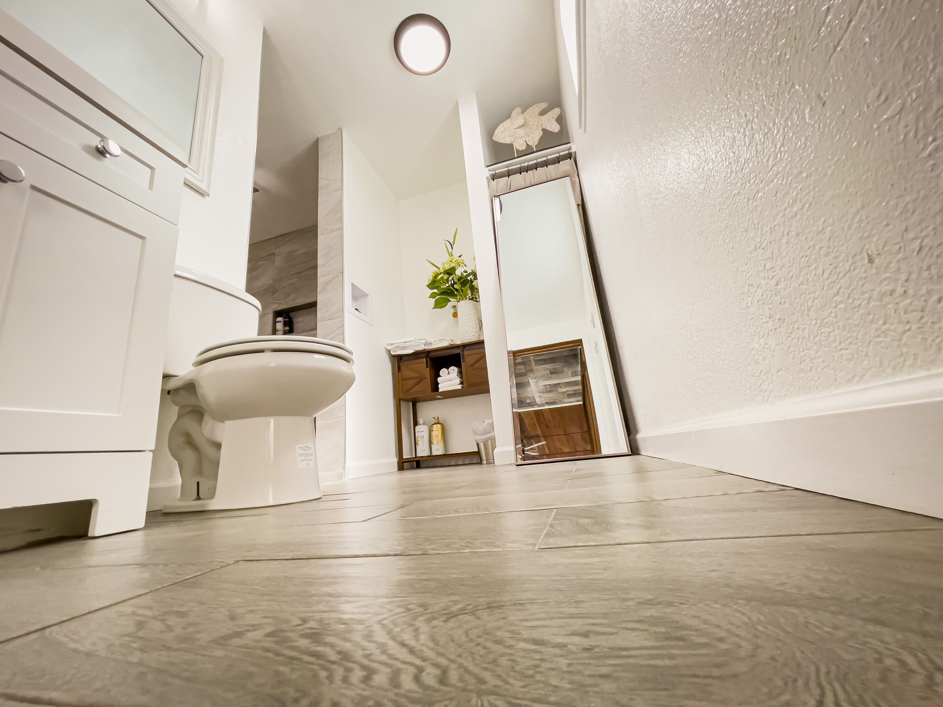 Une salle de bain moderne équipée de toilettes, d’un lavabo et d’un meuble-vasque. On y trouve une étagère avec des articles de toilette et une plante en pot.
