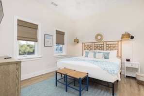 Quarto com cama, mesas de cabeceira, escrivaninha e janela com persianas.