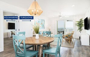 Un coin repas avec des chaises de couleur turquoise et une table en bois, une grande fenêtre offrant une belle vue et un téléviseur en arrière-plan.