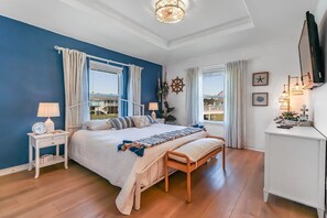 A bedroom with a large bed, a bedside table with a lamp, a bench, and a TV on a stand.