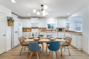 A modern kitchen with white cabinetry, a central island, and a dining area with blue chairs.